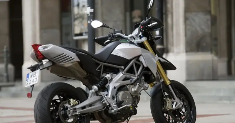 Srebrno-czarny motocykl Aprilia Dorsoduro 750 z żółtymi lagami, gotowy do jazdy po miejskich ulicach.