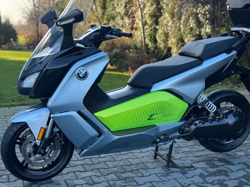 Srebrno-czarny skuter elektryczny BMW C Evolution z zielonym akcentem i napisem "C Evolution" na boku, stojący na chodniku.