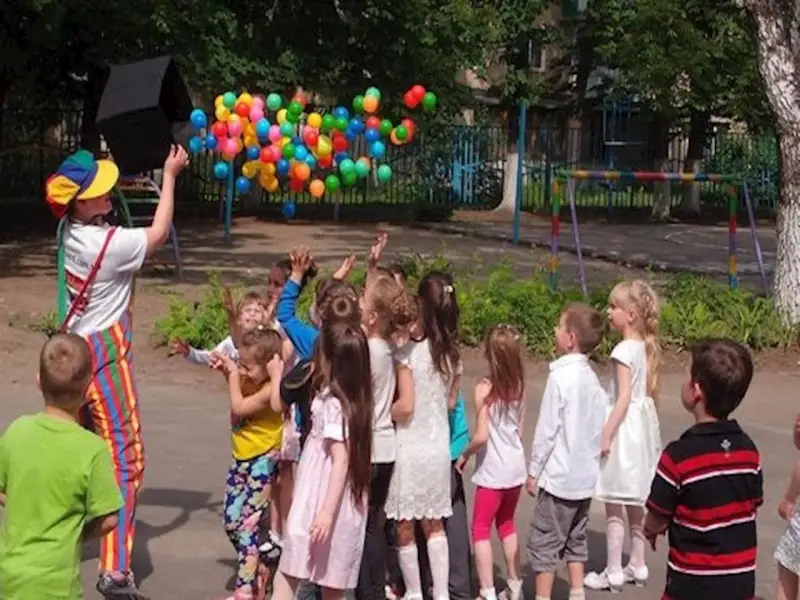 Klaun wypuszcza balony dla dzieci. Czy są zerówki w szkołach? Dzieci cieszą się zabawą na świeżym powietrzu.