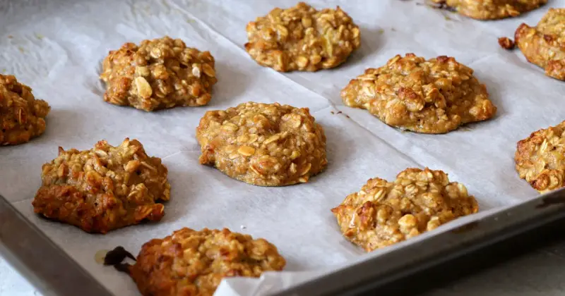 Pyszne, domowe ciastka owsiane z bananem, ułożone na blasze wyłożonej papierem do pieczenia.