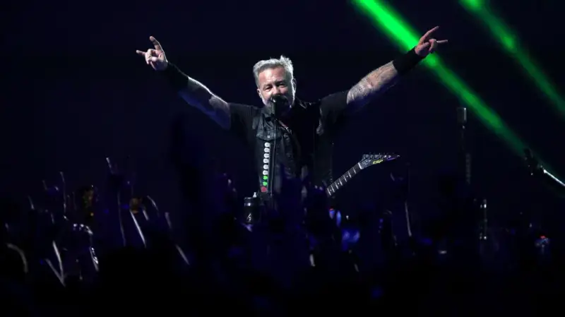 James Hetfield, un des membres de Metallica, salue la foule avec les cornes du diable, éclairé par des faisceaux verts.