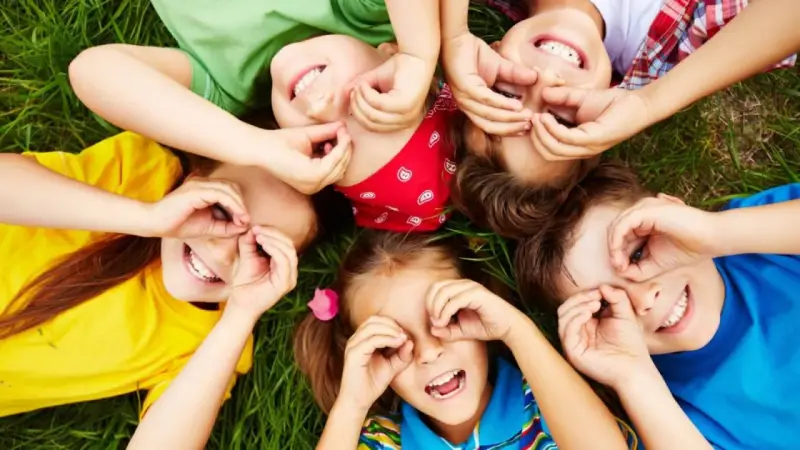 Niños riendo y jugando en el césped, creando formas con sus manos. Sonrisas contagiosas, perfectas para frases para niños.