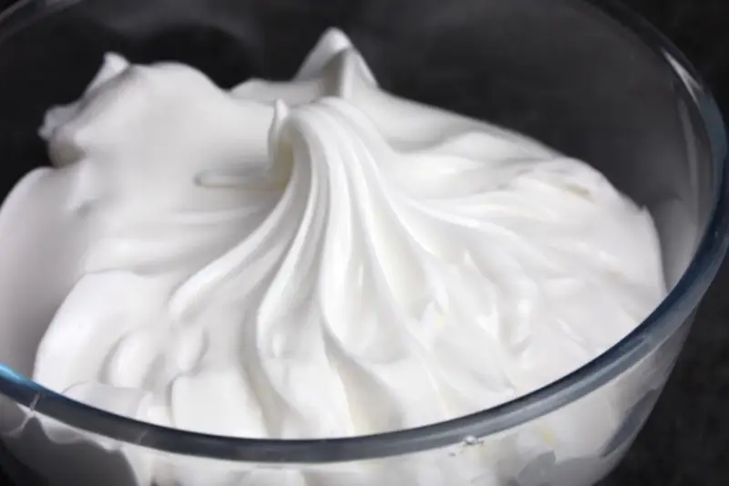 Merengue italiano esponjoso y brillante en un bol de cristal, listo para decorar postres.