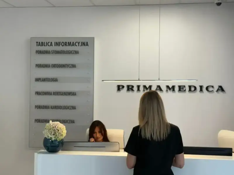 Recepcja gabinetu stomatologicznego Primamedica z tablicą informacyjną i pracownicą.