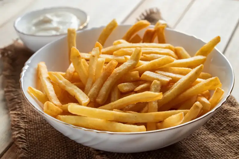 Chrupiące frytki z airfryer w białej misce, obok sos. Idealna przekąska na szybki obiad.