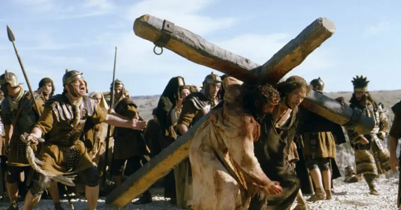 Scena z filmów chrześcijańskich: Jezus dźwigający krzyż, otoczony przez żołnierzy.