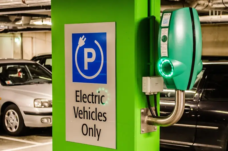 Znak "Tylko pojazdy elektryczne" i zielona ładowarka EVbox. Zastanawiasz się, ile kosztuje ładowanie samochodu elektrycznego w domu?
