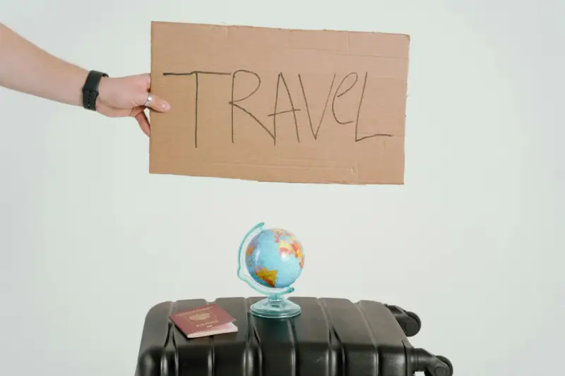 Ręka trzyma tabliczkę z napisem TRAVEL. Obok walizka, globus i paszport. Czy to zapowiedź kolejnych pozytywnych emka travel opinie?