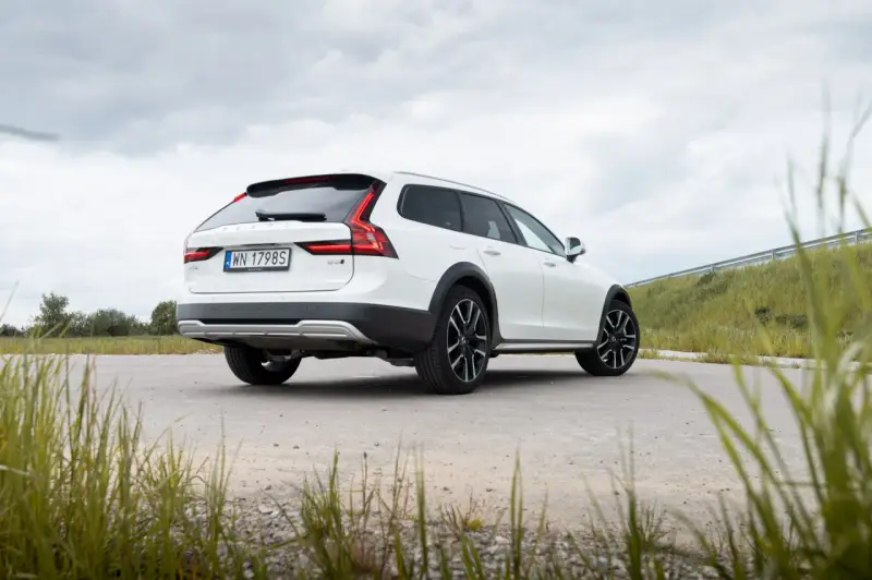 Białe Volvo Cross Country na tle pochmurnego nieba i zielonych wzgórz.