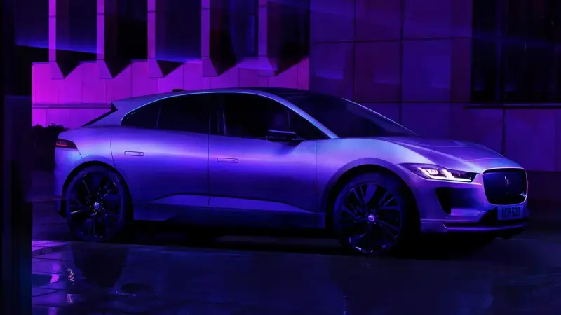 Jaguar I-Pace w fioletowym świetle, zaparkowany na mokrej nawierzchni.