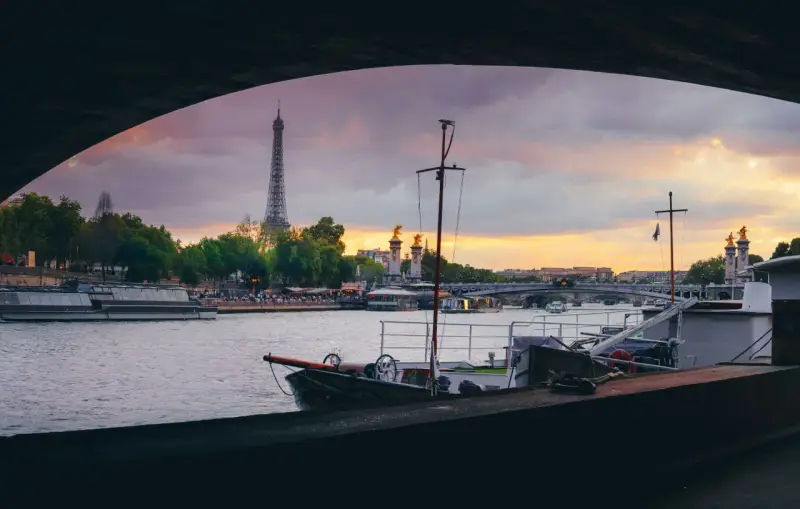 Vue de Paris au coucher du soleil, avec la Tour Eiffel en arrière-plan. Une péniche est amarrée, offrant un aperçu de la vie sur l'eau.