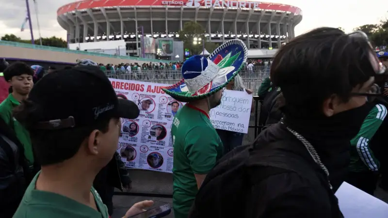 Tłum ludzi przed stadionem Azteca. Na pierwszym planie mężczyzna w meksykańskim kapeluszu, obok baner z portretami zaginionych.