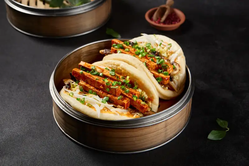 Pierożki baozi z tofu i warzywami, podane w bambusowym parowniku.