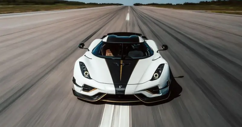 Biały Koenigsegg Regera z czarnym pasem i złotymi akcentami pędzi po pasie startowym, zostawiając za sobą smugę prędkości.
