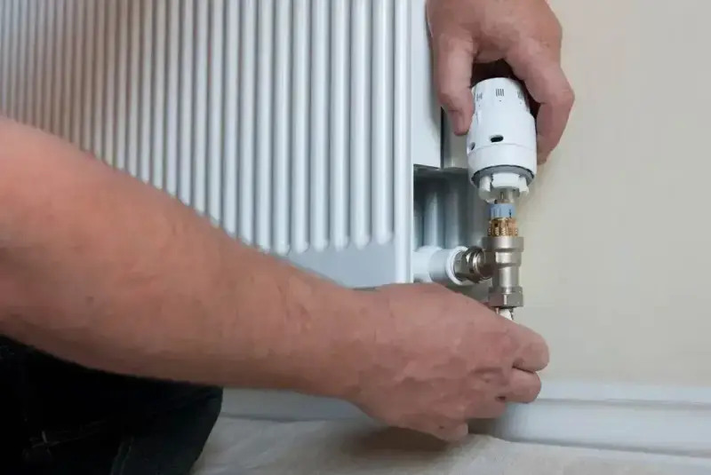 Wymiana zaworu w grzejniku bez spuszczania wody. Ręce majsterkowicza przykręcają nowy zawór termostatyczny.