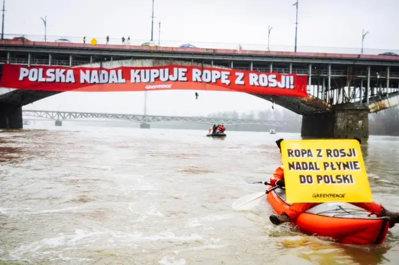 Na moście Poniatowskiego wisi czerwony baner "Polska nadal kupuje ropę z Rosji!". Kajakarz Greenpeace na Wiśle trzyma żółtą tablicę "Ropa z Rosji nadal płynie do Polski".