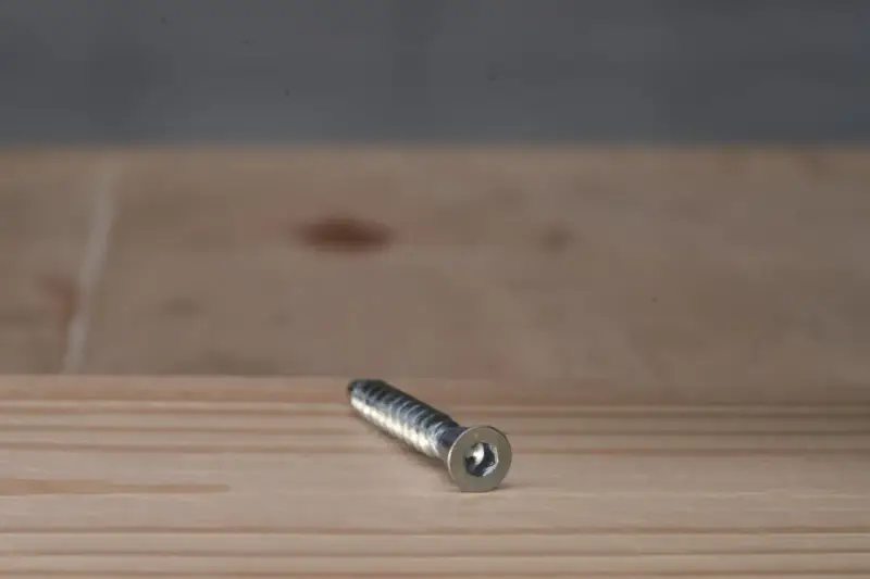 Metalowy konfirmat z gniazdem sześciokątnym leży na drewnianej powierzchni.
