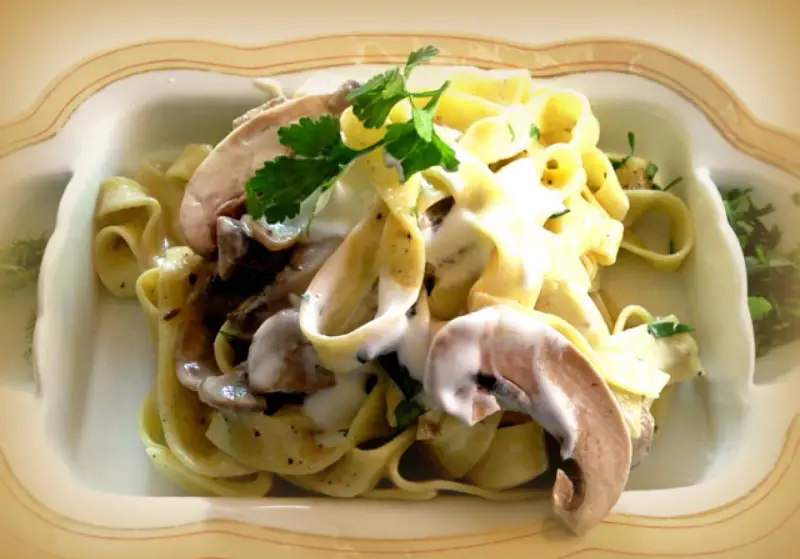 Pyszne tagliatelle z grzybami w kremowym sosie, udekorowane natką pietruszki.