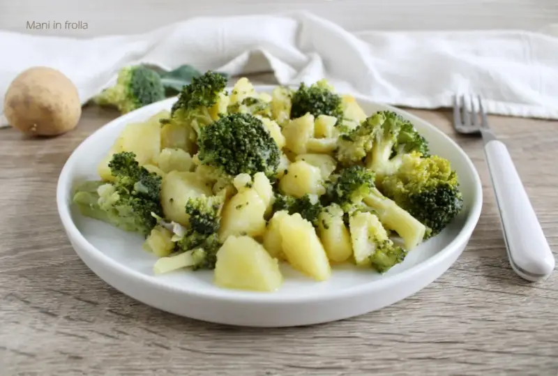 Un plato de brócoli con patatas, sencillo y saludable. Una patata entera y trozos de brócoli reposan cerca.