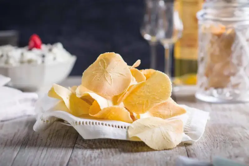 Delicati cialde, un dolce tipico toscano, su un tovagliolo ricamato. Sullo sfondo, una ciotola con crema e bicchieri.