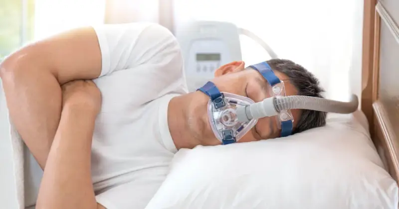 Mężczyzna śpi z maską CPAP, która pomaga mu oddychać podczas bezdechu sennego.