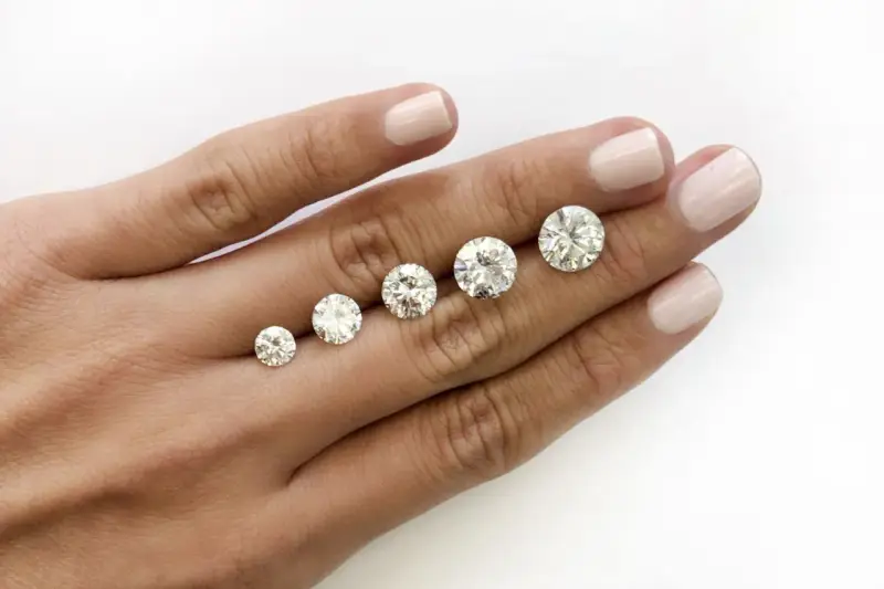 Five round brilliant cut diamonds are displayed on a hand, showing a progression in size. The largest diamond is what is considered a big diamond.