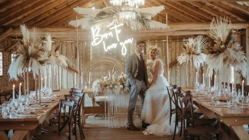 Elegancka sala weselna stodoła z parą młodą, neonem "Born to love you" i boho dekoracjami z traw pampasowych.