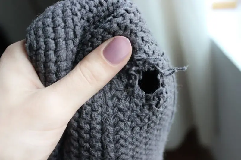 Dito un buco in un maglione grigio, pronto per imparare come rammendare uno strappo a mano.
