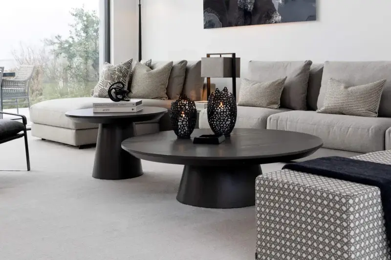 Ett modernt vardagsrum med en stor, mörk soffa och ett elegant, runt soffbord. Två svarta ljuslyktor står på soffbordet.
