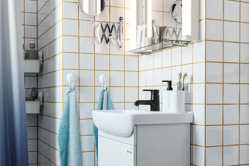 Salle de bain moderne avec carrelage blanc joint gris, lavabo, robinetterie noire et accessoires pratiques.