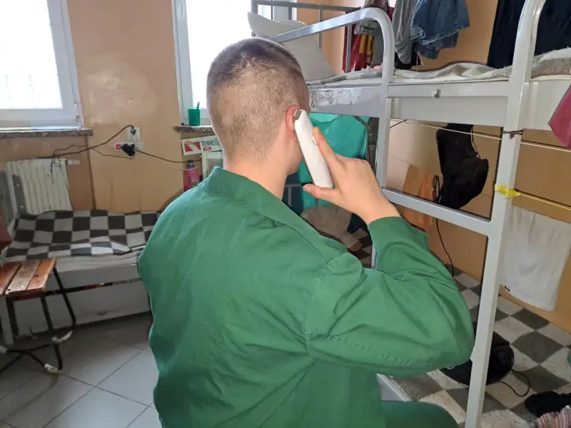 Mężczyzna w zielonym uniformie rozmawia przez telefon. Czeka na odpowiedni moment, po jakim czasie więzień może dzwonić do rodziny.