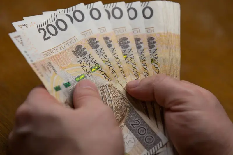 Dłonie trzymają stos banknotów po 200 zł. Czy to wystarczy, by poznać, ile wynosi najniższa krajowa netto?