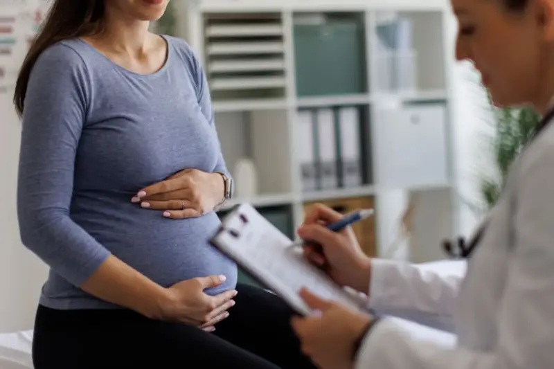 Visita medica: una donna incinta tiene la pancia mentre il medico annota sul foglio, forse il tracciato delle contrazioni preparatorie.