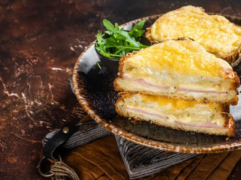 Deux croque monsieur bechamel dorés, garnis de jambon et de fromage fondant, servis avec une salade verte.