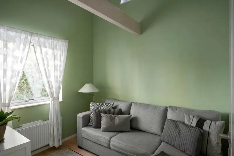 Sofá gris con cojines, lámpara y cortinas blancas junto a pared verde. ¡Excelentes ideas pintar casa con este tono fresco!