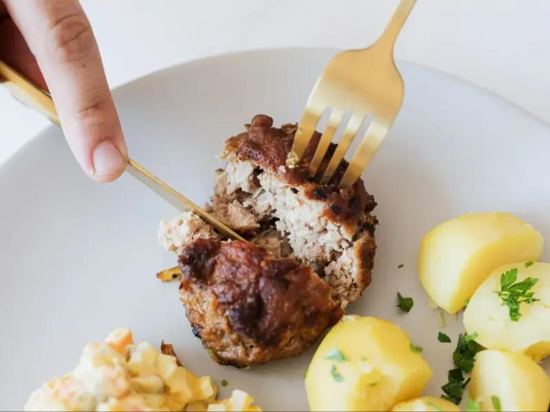 Kotlety mielone przepis babci: soczysty kotlet rozkrajany widelcem, obok ziemniaczki i surówka.