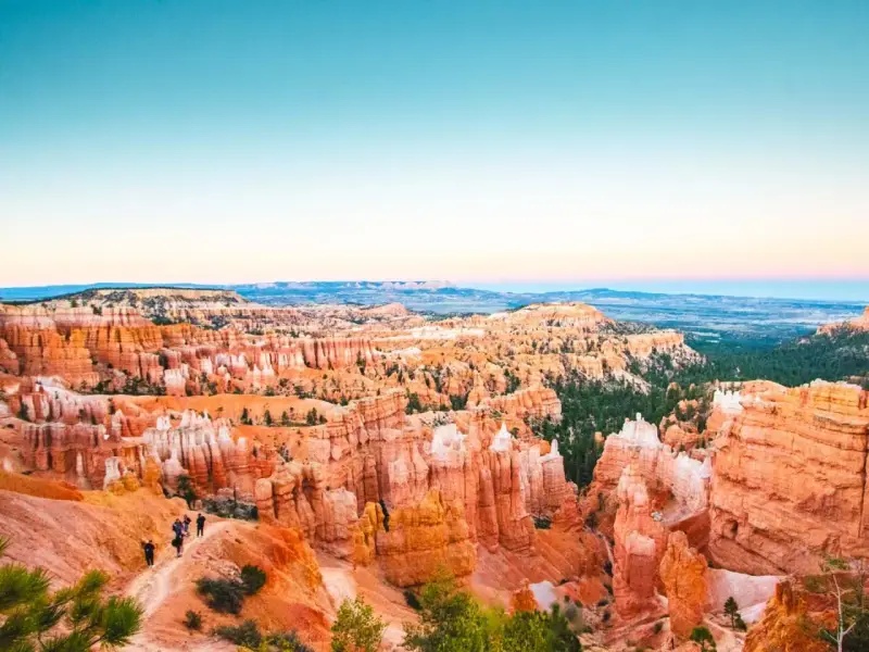 Zachód słońca nad Bryce National Park. Wąwóz pełen pomarańczowych hoodoos i zielonych drzew, z turystami na szlaku.