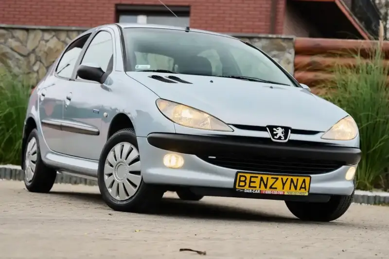 Jasny Peugeot 206 1.4 benzyna z żółtą tablicą "BENZYNA" na zderzaku, zaparkowany na zewnątrz.