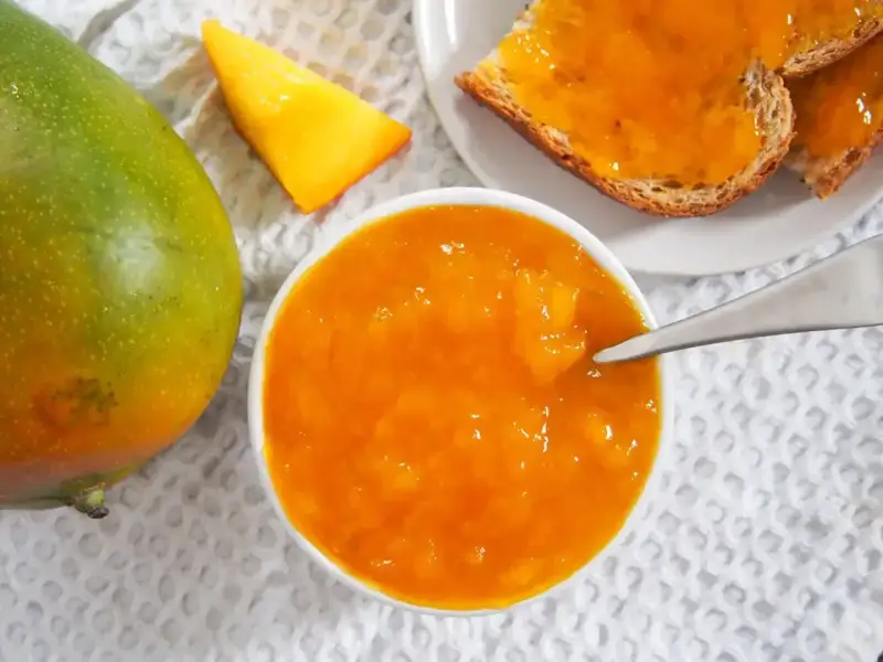 Słoik z dżemem z mango, obok świeży owoc i kromki chleba. Codzienne jedzenie mango to pyszny początek dnia.