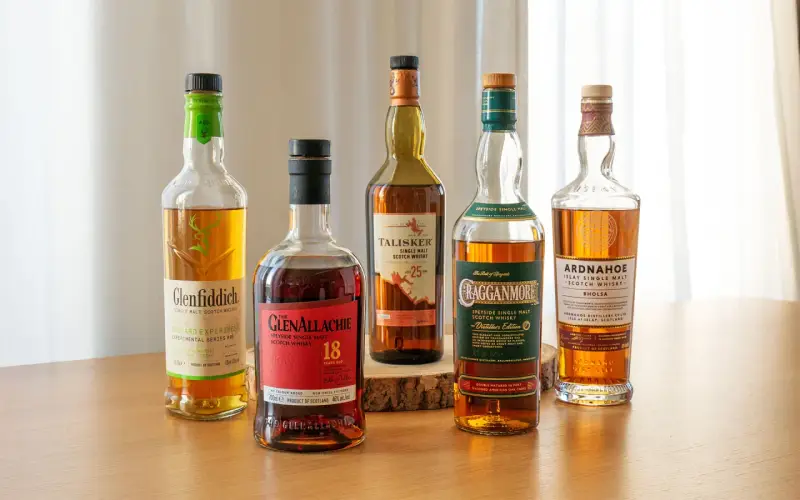 Fünf Flaschen gute Whiskey-Sorten: Glenfiddich, Glenallachie, Talisker, Cragganmore und Ardnahoe stehen auf einem Holztisch.