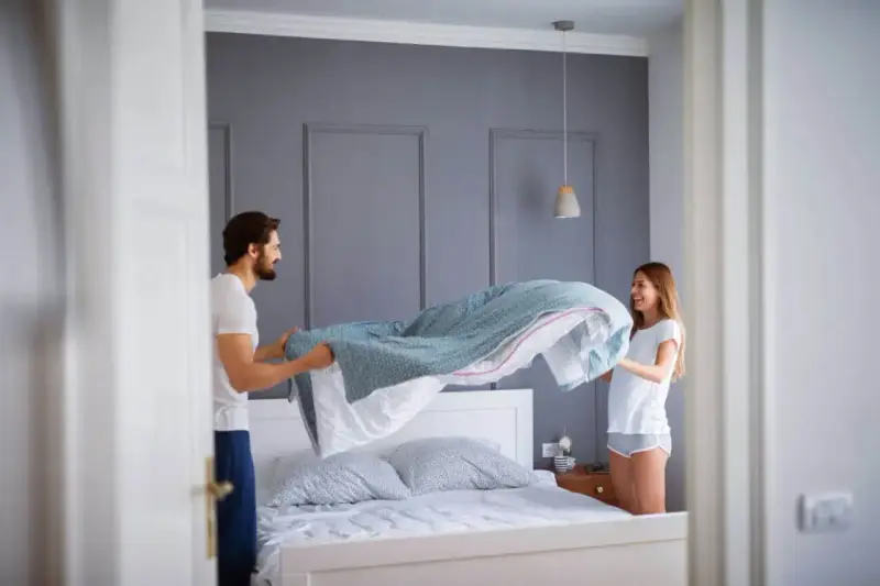 Coppia felice che cambia le lenzuola, un gesto che ci ricorda ogni quanto cambiare le lenzuola per un sonno più sano.