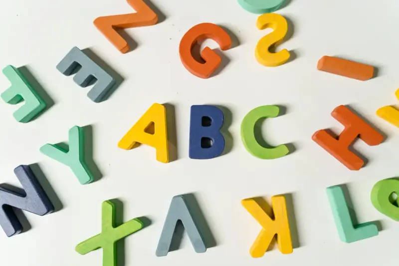 Kolorowe drewniane litery, idealne dla nauczyciela wychowania przedszkolnego, tworzą napis "ABC" i inne znaki.