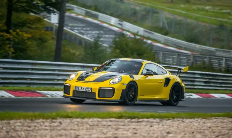 Żółty Porsche 911 GT2 RS z czarnymi pasami pędzi po torze wyścigowym.