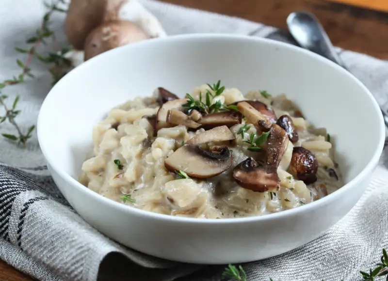 Kremowe risotto z pieczarkami i świeżym tymiankiem w białej misce.
