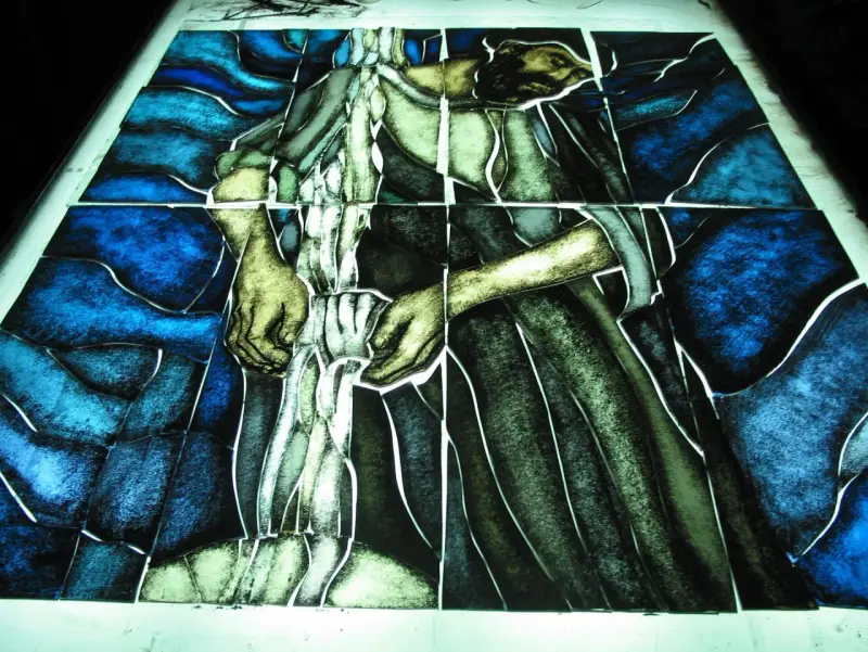 Fragment witrażu w stylu modernizm, przedstawiający postać w niebieskim i zielonym tle.