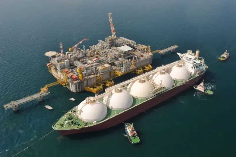Praca na statku LNG: potężna jednostka z kopułami ładunkowymi przy platformie wydobywczej, holowniki asystują.