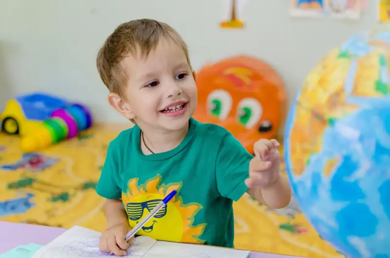 Uśmiechnięte polskie dziecko w hiszpańskiej szkole bawi się globusem i rysuje w zeszycie.