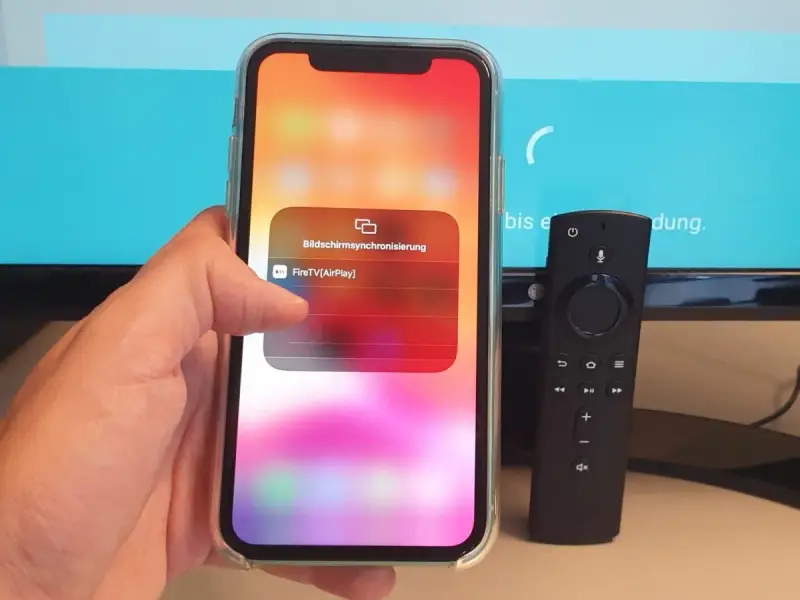 iPhone mit Fire TV Stick verbinden: AirPlay-Option wird auf dem iPhone angezeigt, daneben liegt die Fire TV Fernbedienung.