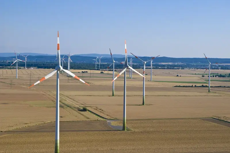 Großer onshore windpark in einer weiten Feldlandschaft unter blauem Himmel.