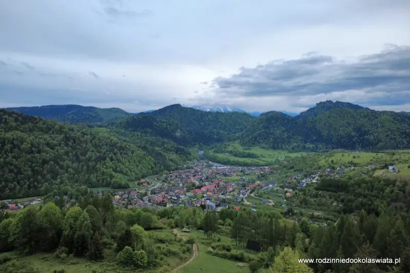 Widok na malowniczą dolinę z miasteczkiem Szczawnica. W oddali góry, a na pierwszym planie zielone wzgórza. To idealne miejsce na odkrywanie szczawnickich atrakcji.